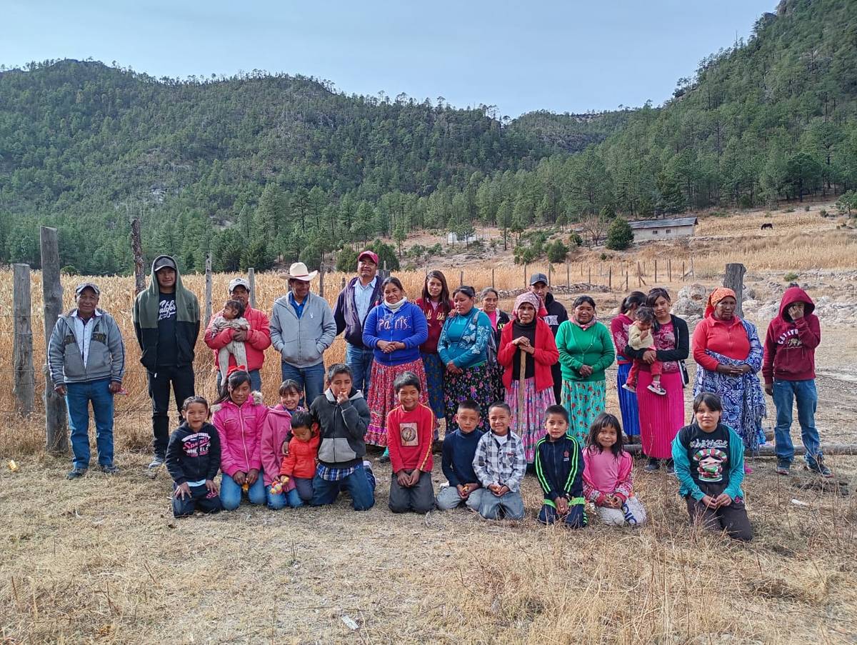 Integrantes de un grupo de ahorro de la Sierra, con niños al frente y cerros con pinos al fondo